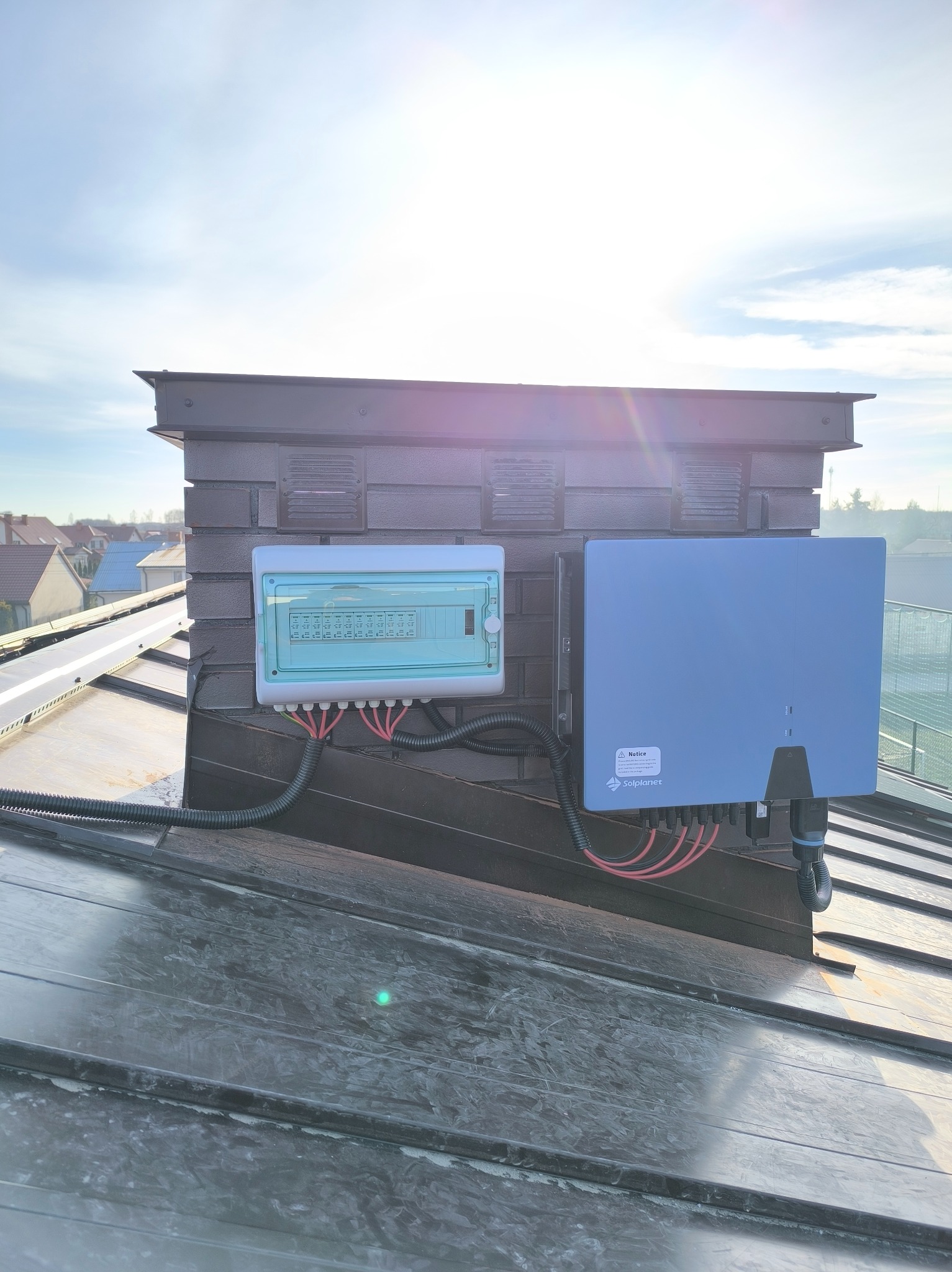 Zamontowana instalacja fotowoltaiczna na dachu, widoczna skrzynka elektryczna i inwerter Solplanet, kable poprowadzone w peszlu. Lekkie zachmurzenie.