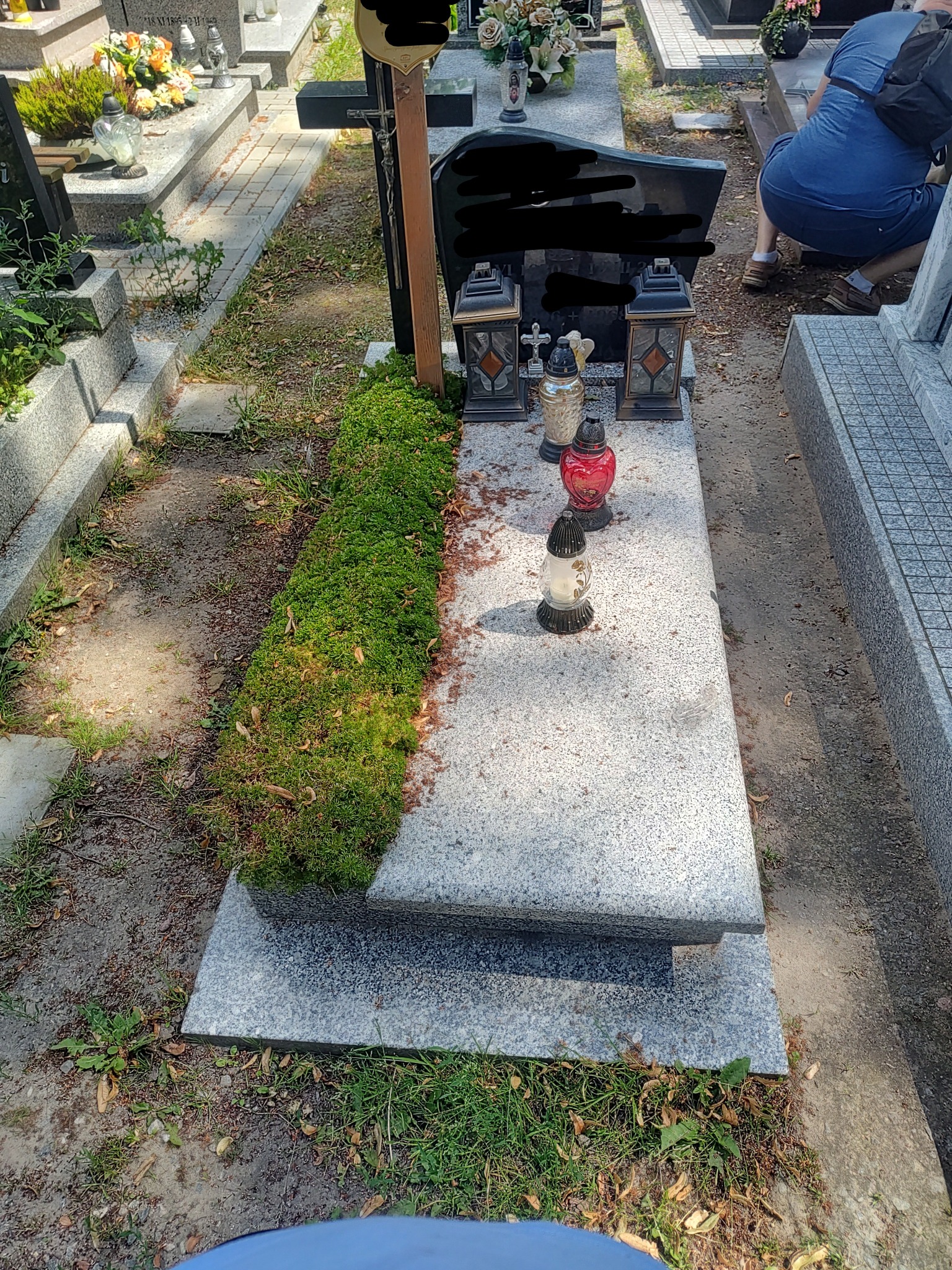 Granitowy nagrobek z mchem, lampionami i zniczami, widok z góry.