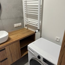 Serhii Diachenko - Nowoczesna łazienka z drewnianą szafką pod umywalką, grzejnikiem drabinkowym i białą pralką.