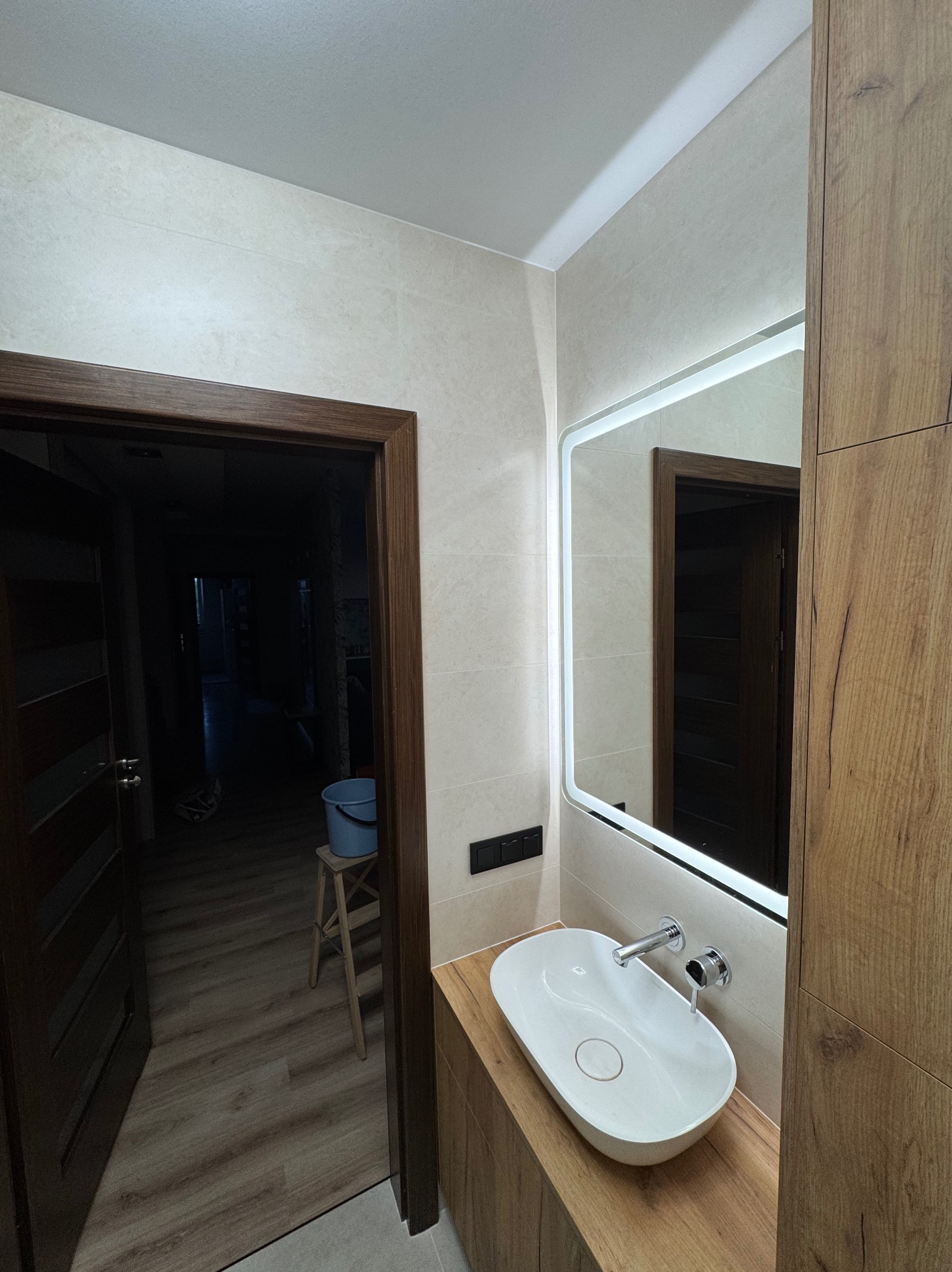 Nowoczesna łazienka: owalna umywalka nablatowa, lustro z podświetleniem LED, drewnopodobna zabudowa i beżowe płytki. Minimalistyczny design.