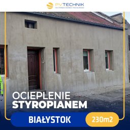 PV TECHNIK SPÓŁKA Z OGRANICZONĄ ODPOWIEDZIALNOŚCIĄ - Dom jednorodzinny w trakcie ocieplania styropianem, widoczne okna zabezpieczone folią, surowa elewacja przed nałożeniem tynku. Na górze logo firmy PVTechnik.