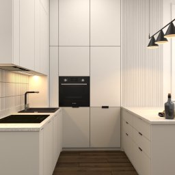 Gawron Studio Design - Nowoczesna, minimalistyczna kuchnia w odcieniach bieli z drewnianą podłogą, oświetlona trzema czarnymi lampami wiszącymi, z dekoracyjnymi akcentami w postaci butelki wina i słoika na blacie.