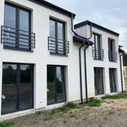 Elewacja nowo wybudowanego, dwukondygnacyjnego domu z czarnymi oknami i minimalistycznymi, poziomymi barierkami balkonowymi z metalowych profili.