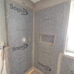 Usługi glazurnicze i remontowo budowlane JG - Przygotowanie ścian w kabinie prysznicowej do położenia płytek, widoczna warstwa hydroizolacji z logo Sopro, wnęka w ścianie, częściowo wykończona ściana mozaiką.