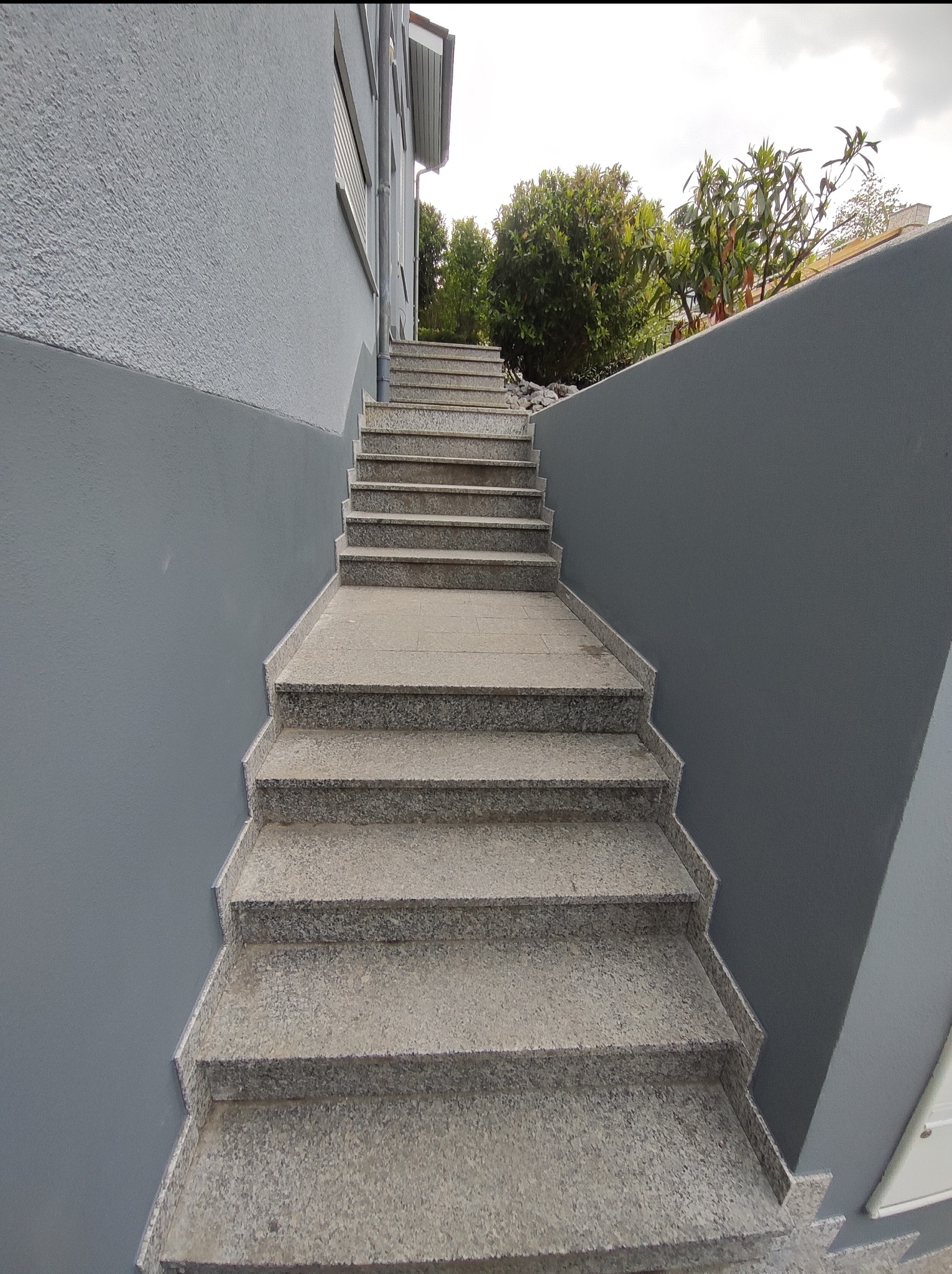 Zewnętrzne schody z szarego granitu prowadzące w górę, z widocznymi ścianami pomalowanymi na szaro i zielenią w tle.