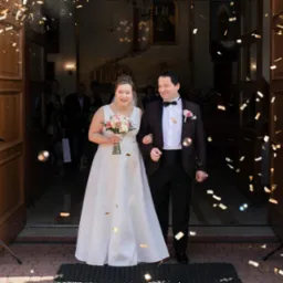 Para młoda, wychodząca z kościoła w Rudzie Śląskiej, obsypywana konfetti, z uśmiechami na twarzach i bukietem w ręku panny młodej, w tle widoczni goście.