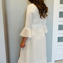 Anna's Fashion - Kobieta w długiej, białej sukience z falbankami i rękawami typu dzwonek, widok z tyłu, z rozpuszczonymi, brązowymi włosami.