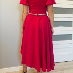 Anna's Fashion - Kobieta w fuksjowej sukience z asymetrycznym dołem, ozdobnym paskiem i brokatowych szpilkach, widziana od tyłu na tle białych drzwi.