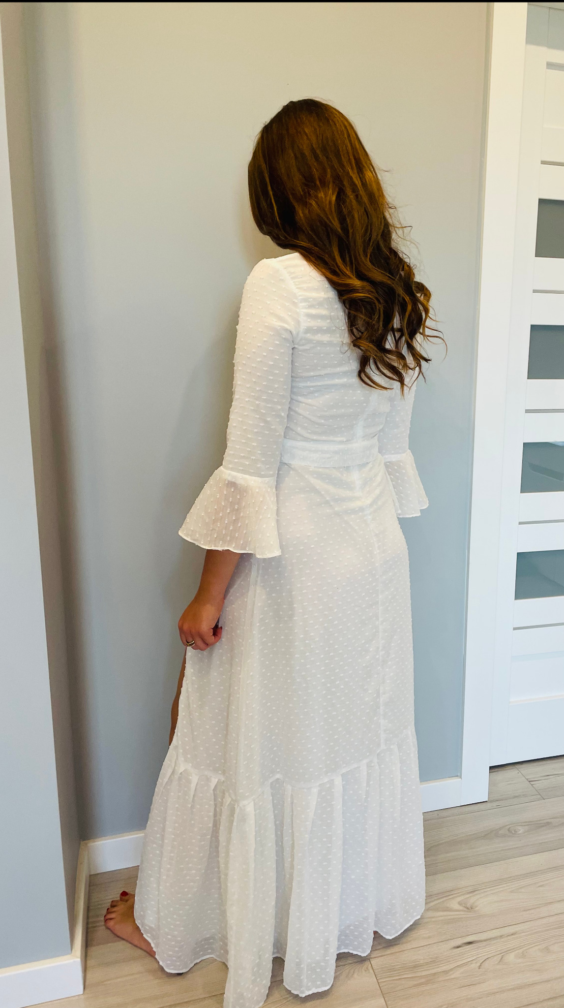 Kobieta w długiej, białej sukience z falbankami i rękawami typu dzwonek, widok z tyłu, z rozpuszczonymi, brązowymi włosami.