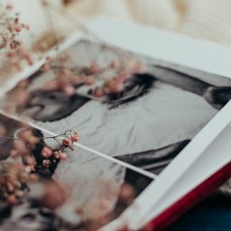 Weronika Zelewska Fotografia-Usługi Fotograficzne - Otwarty album ze zdjęciem czarno-białym przedstawiającym parę, ozdobiony delikatnymi, zasuszonymi kwiatami w odcieniach różu, leżący na miękkim, kremowym swetrze.