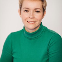 Weronika Zelewska Fotografia-Usługi Fotograficzne - Portret uśmiechniętej kobiety z krótkimi blond włosami, ubrana w zielony golf na jasnym tle.