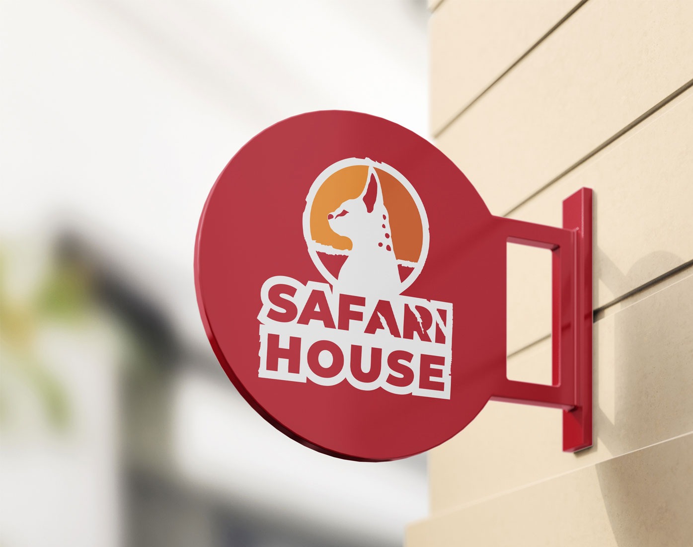 Okrągły, czerwony szyld z białym napisem SAFARI HOUSE i sylwetką psa w pomarańczowym okręgu, zamocowany na beżowej ścianie.
