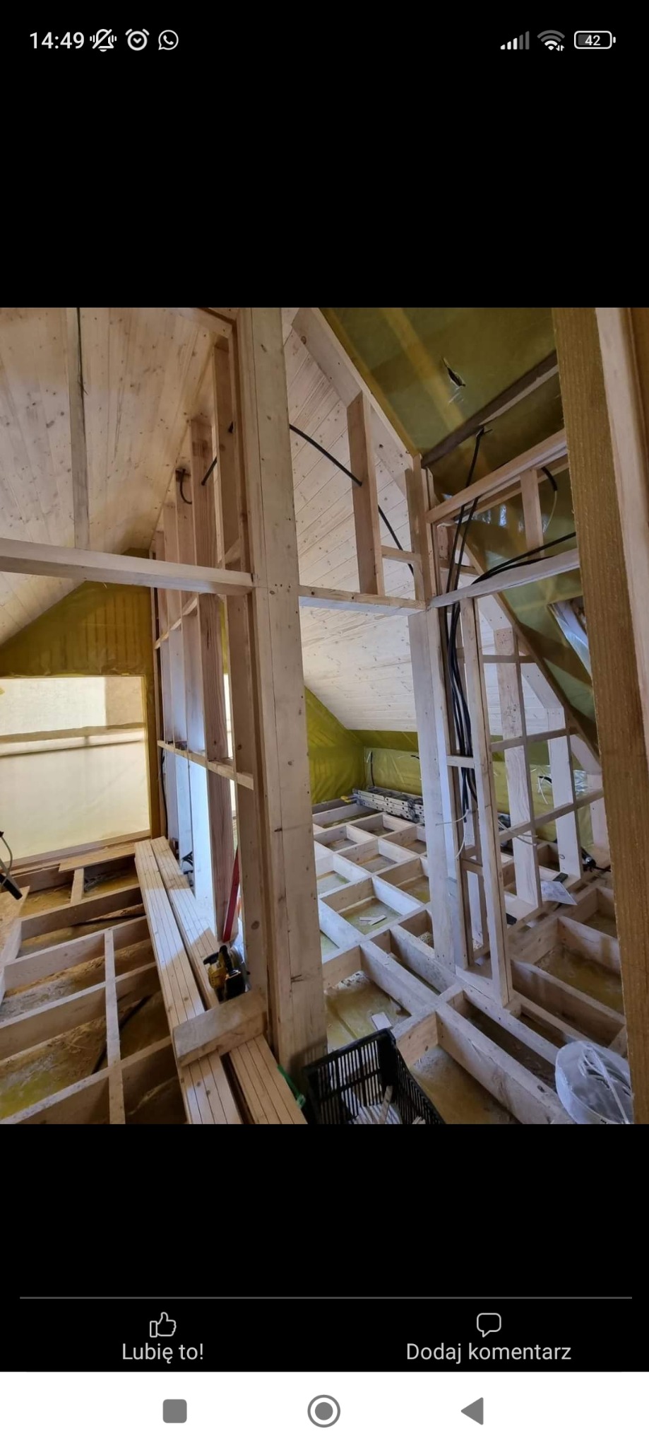 Konstrukcja drewniana poddasza w trakcie budowy, widoczne belki stropowe, ściany szkieletowe, przewody elektryczne i żółta folia izolacyjna.