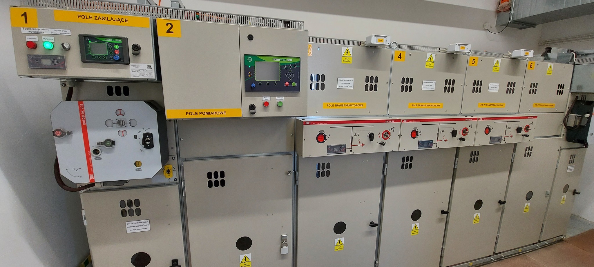 Rozdzielnica elektryczna z modułami zasilającymi, pomiarowymi i transformatorowymi, oznaczona numerami od 1 do 6, z widocznymi panelami sterowania, wskaźnikami i tabliczkami ostrzegawczymi.