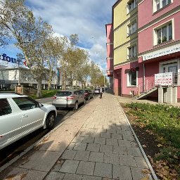 Itludek Michał Osuch - Budynek z szyldem 'Serwis Laptopów, Kasy Fiskalne' w słoneczny dzień na tle ulicy z zaparkowanymi samochodami i budynkiem Carrefour w oddali.