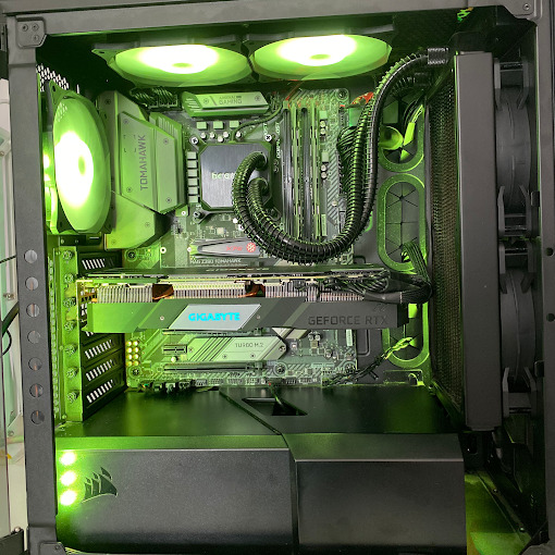 Wnętrze komputera stacjonarnego z podświetleniem LED w odcieniach zieleni, widoczna karta graficzna Gigabyte GeForce RTX, płyta główna Tomahawk, chłodzenie wodne procesora Be Quiet! i wentylatory...