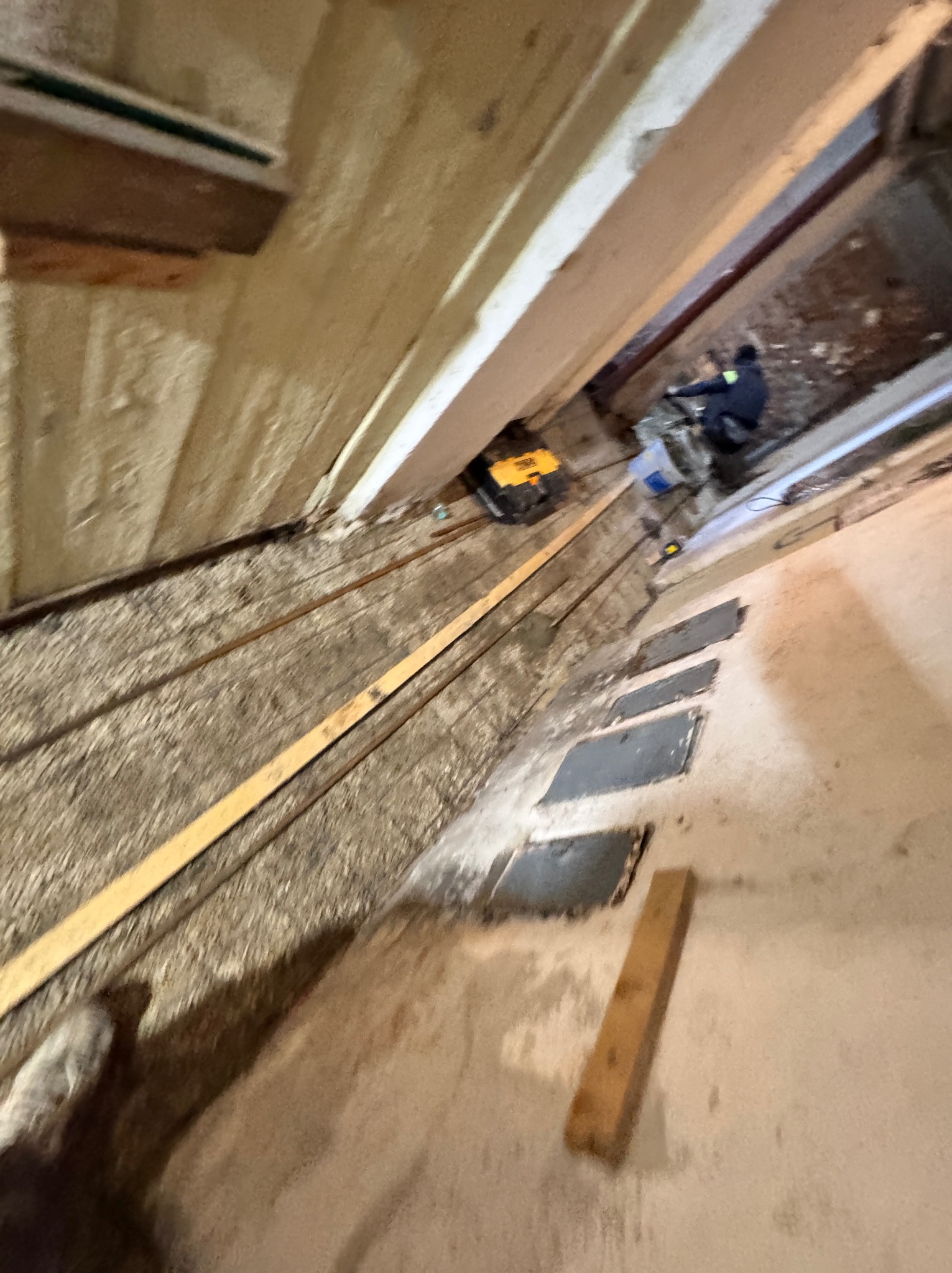 Wnętrze w trakcie prac, widoczna warstwa izolacyjna, narzędzia i pracownik w oddali, ujęcie z dołu.