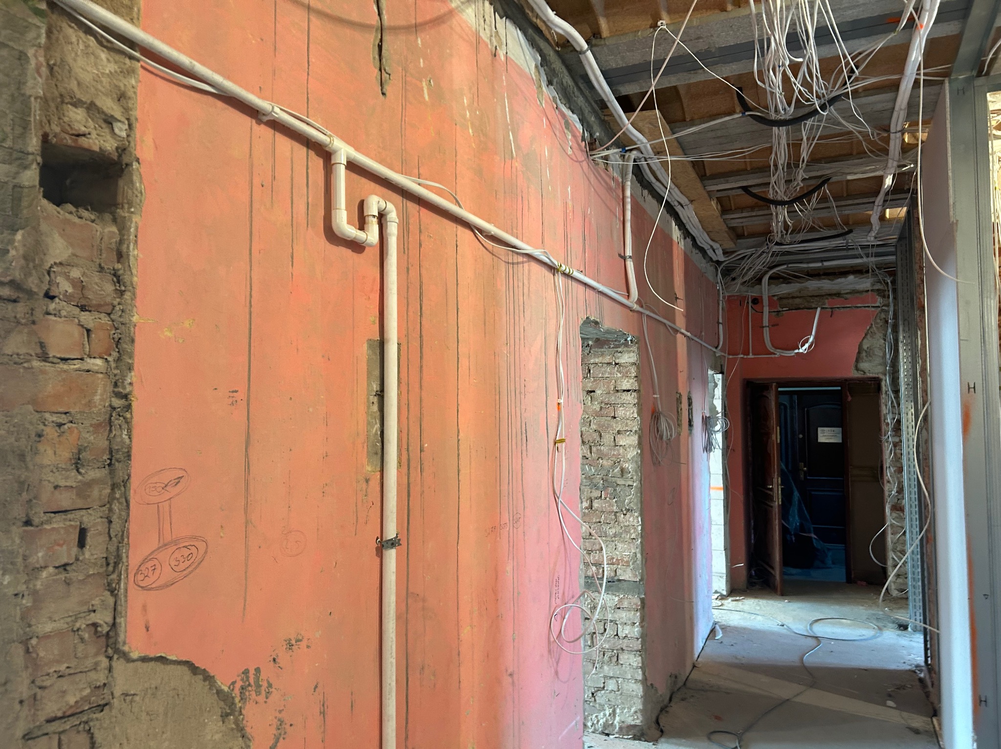 Wnętrze w trakcie remontu: instalacja rur i kabli na ścianach z czerwonej cegły, widoczne przewody pod sufitem, surowy stan wykończenia.