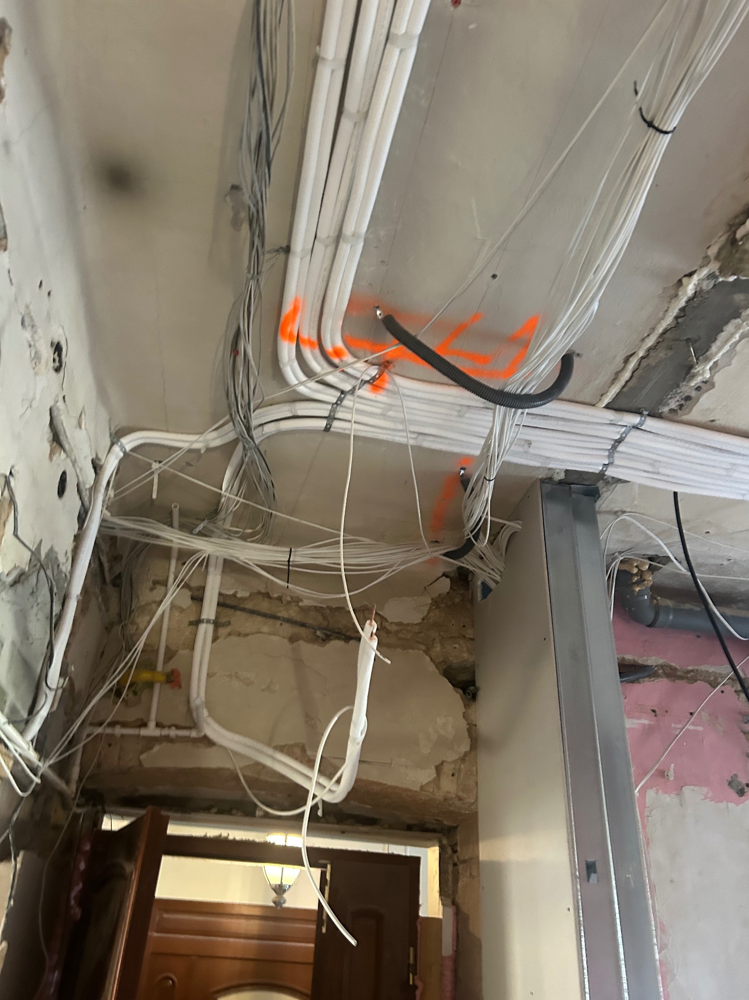 Instalacja przewodów wentylacyjnych i elektrycznych na suficie w trakcie remontu. Widoczne rury wentylacyjne, kable elektryczne i fragmenty sufitu z uszkodzonym tynkiem.