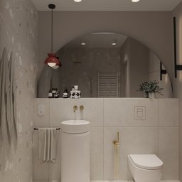 Aurum Studio - Pracownia projektowania wnętrz, Joanna Baracz - Stylowa łazienka z umywalką wolnostojącą, minimalistyczną toaletą i dużym, łukowym lustrem. Uwagę zwracają złote detale armatury i lampa wisząca w kolorze czerwonym.