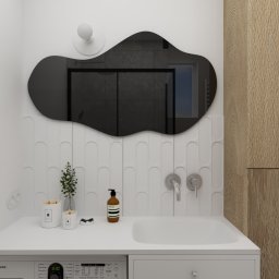 Aurum Studio - Pracownia projektowania wnętrz, Joanna Baracz - Minimalistyczna łazienka z asymetrycznym lustrem, białą umywalką w blacie i pralką. Na blacie dekoracje i kosmetyki. W lustrze odbicie kabiny prysznicowej.