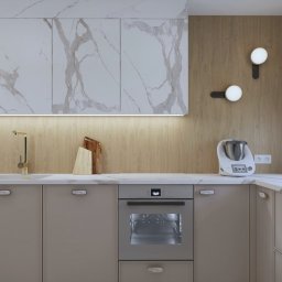 Aurum Studio - Pracownia projektowania wnętrz - Elegancka kuchnia z marmurowymi szafkami górnymi, beżowymi szafkami dolnymi i złotą armaturą. Na blacie stoi robot kuchenny Thermomix.