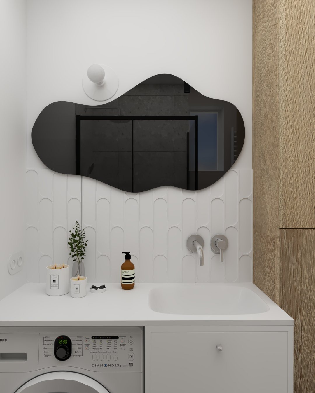 Minimalistyczna łazienka z asymetrycznym lustrem, białą umywalką w blacie i pralką. Na blacie dekoracje i kosmetyki. W lustrze odbicie kabiny prysznicowej.