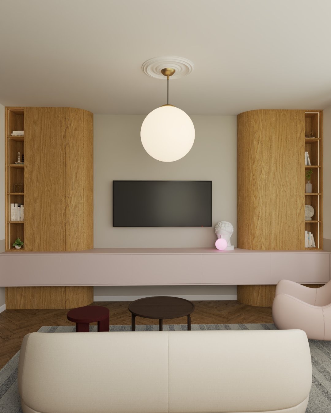 Jasne wnętrze salonu z drewnianymi regałami, niską szafką RTV w pastelowym różu i okrągłą lampą sufitową. Minimalistyczny design z akcentami dekoracyjnymi.