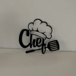 Czarny, wycięty laserowo napis 'Chef' z czapką kucharską i łopatką, umieszczony na jasnym tle.