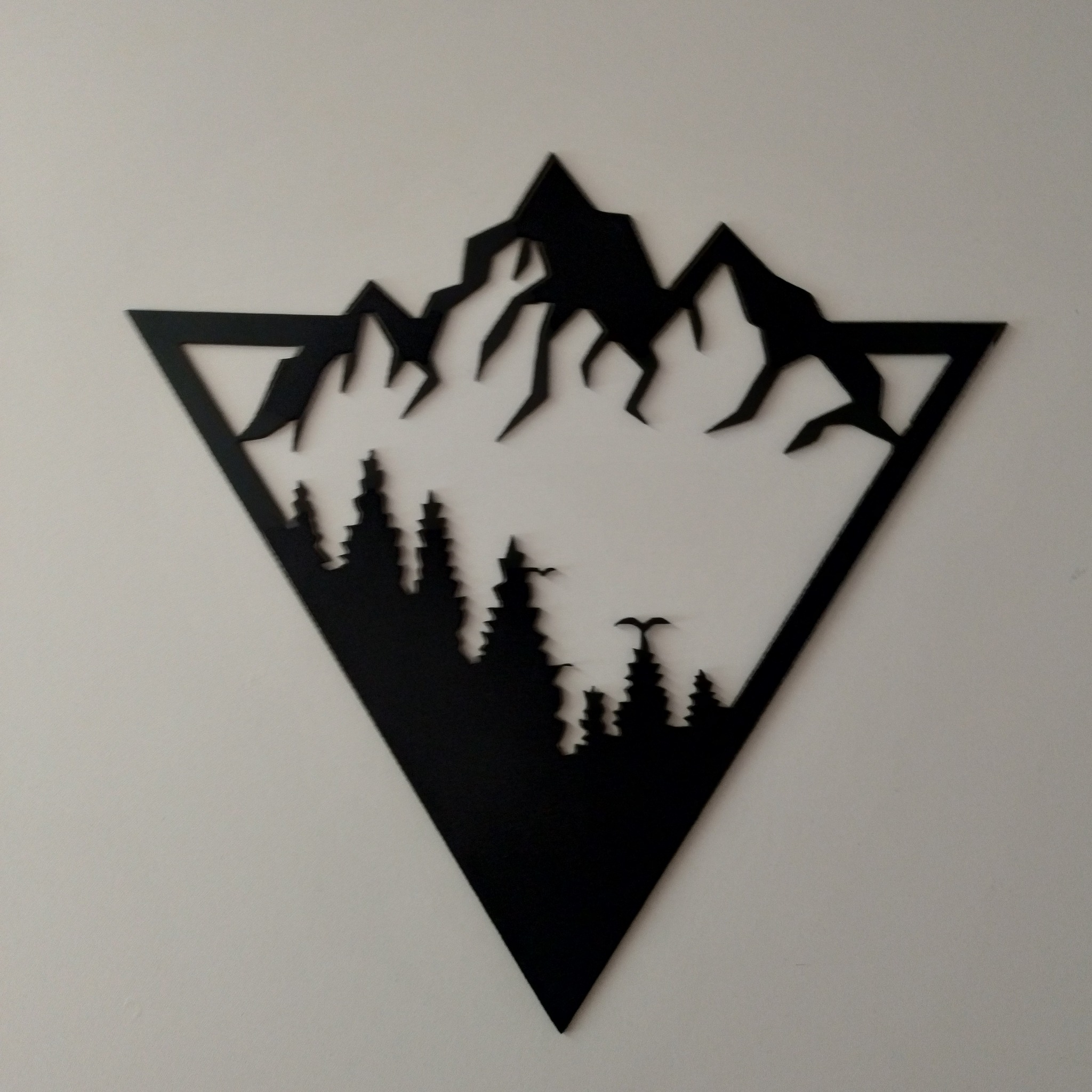 Czarna, metalowa ozdoba ścienna przedstawiająca górski krajobraz w trójkątnej ramie, z motywem górskich szczytów i sylwetek drzew iglastych.