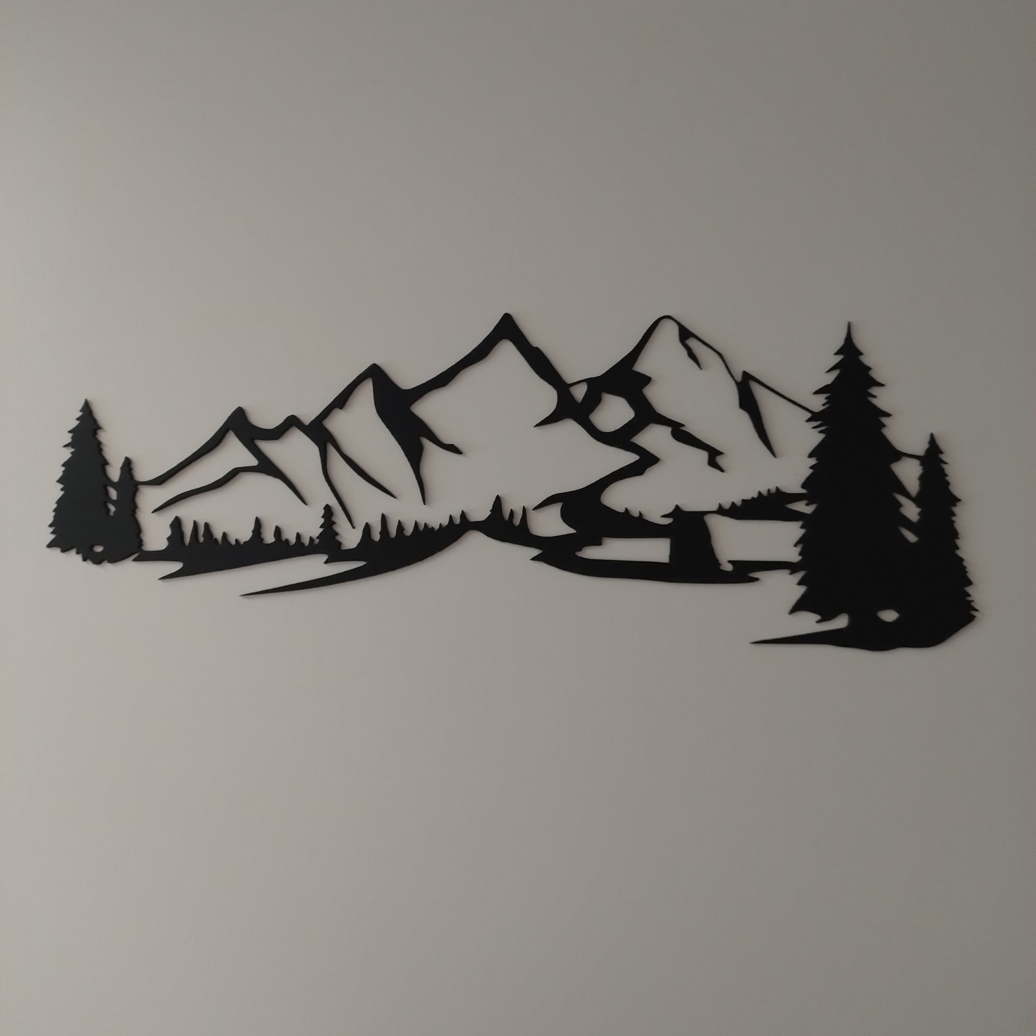 Metalowa dekoracja ścienna przedstawiająca sylwetkę górskiego krajobrazu z drzewami iglastymi, wykonana prawdopodobnie metodą cięcia laserowego.