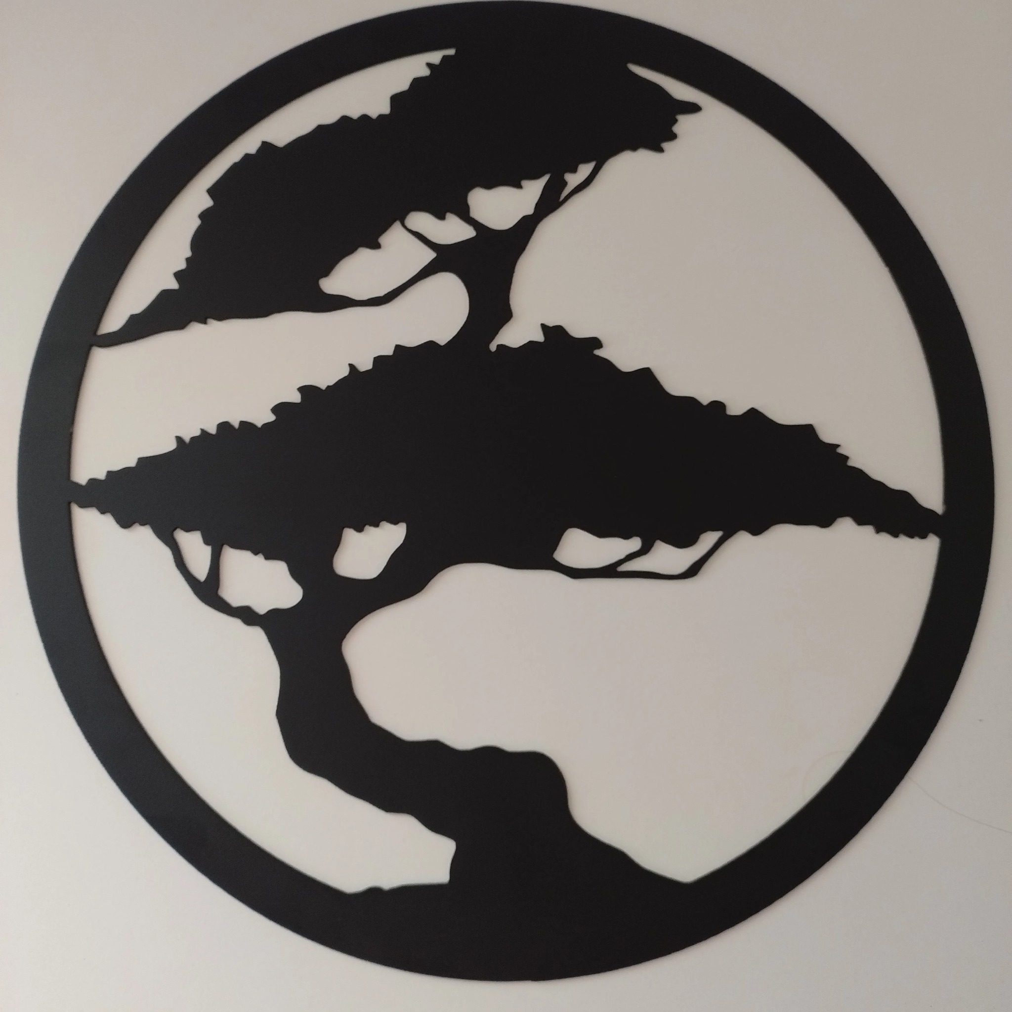 Wycięta laserowo z metalu dekoracja ścienna przedstawiająca stylizowane drzewko bonsai w okręgu.