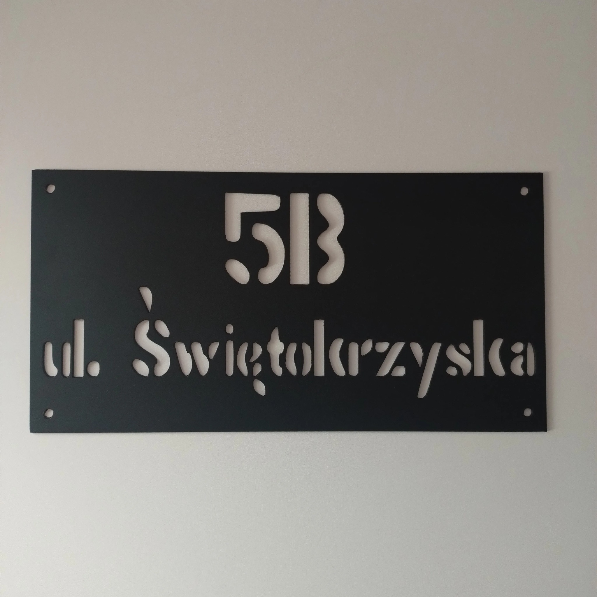 Czarna tabliczka z wyciętym laserowo adresem 'ul. Świętokrzyska 51B', wykonana w Górnie i zamontowana na jasnej ścianie.