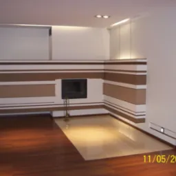 Nowoczesny salon z wykończonym kominkiem w poziome pasy brązowo-białe, kontrastujący z ciemną podłogą i białymi ścianami, oświetlenie punktowe.