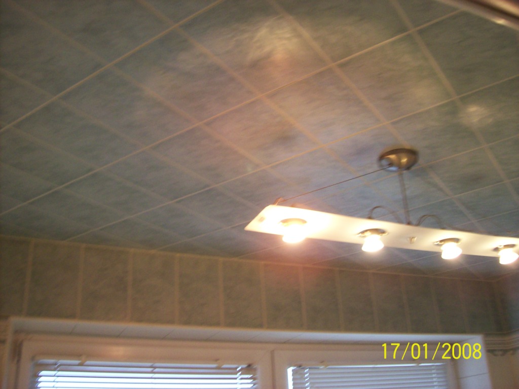 Wykończone wnętrze łazienki z zielonymi płytkami na ścianach i suficie, oświetlone przez podłużną lampę z czterema żarówkami, widok na okno z żaluzjami.