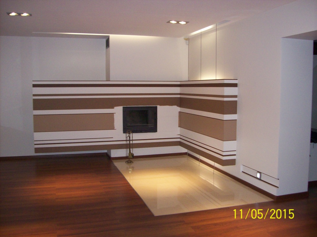 Nowoczesny salon z wykończonym kominkiem w poziome pasy brązowo-białe, kontrastujący z ciemną podłogą i białymi ścianami, oświetlenie punktowe.