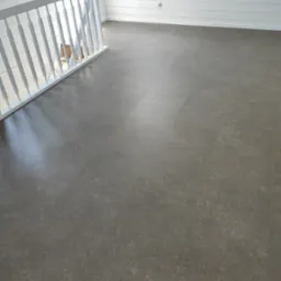 Szara, matowa podłoga z paneli winylowych w nowym pomieszczeniu z białą boazerią i białą balustradą schodów.