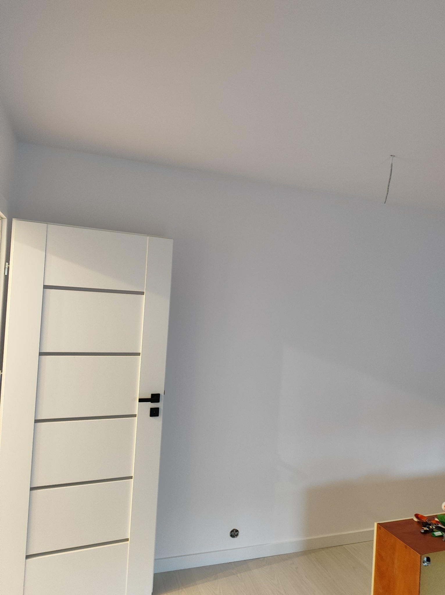 Białe, nowoczesne drzwi wewnętrzne z poziomymi frezowaniami i czarną klamką w nowo wykończonym pokoju w Świnoujściu, widoczny fragment ściany i sufitu z wystającym kablem.