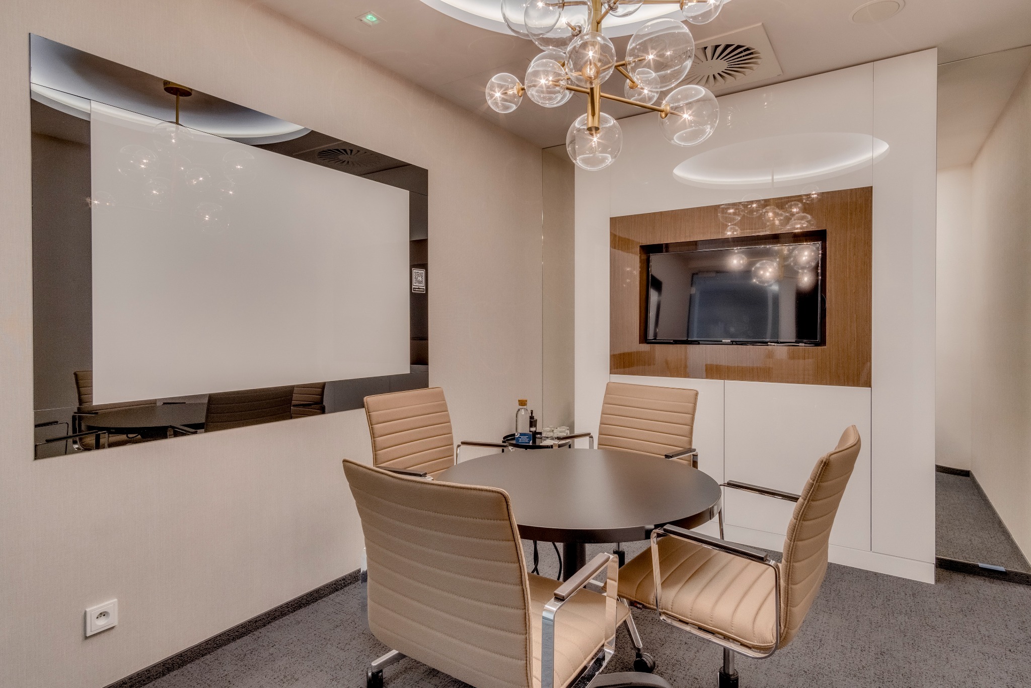 Nowoczesna sala konferencyjna w wirtualnym biurze w Warszawie, z okrągłym stołem, beżowymi krzesłami na kółkach, dużym lustrem i designerską lampą sufitową.