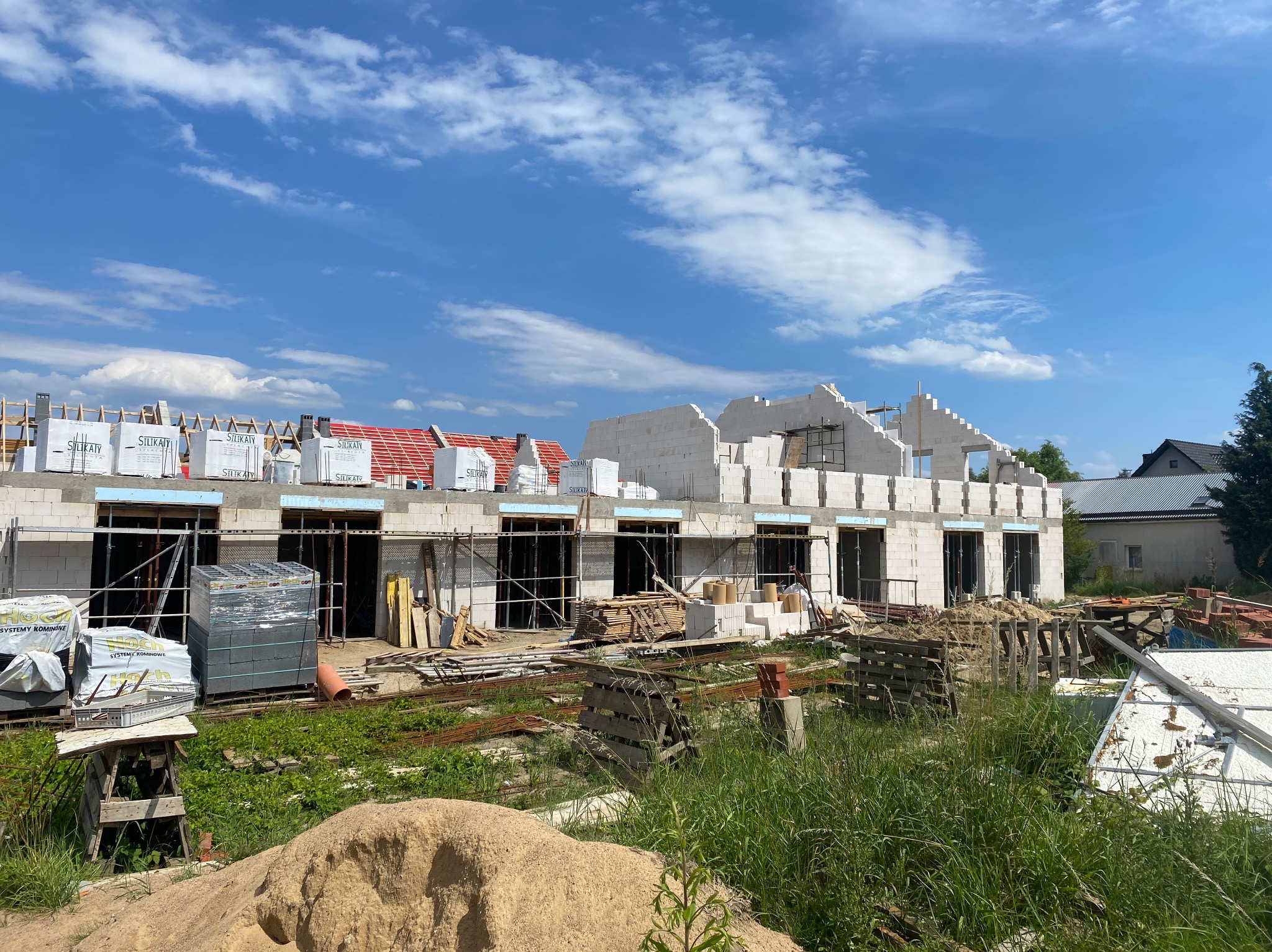 Budowa domu murowanego w trakcie wznoszenia ścian z bloczków Silka, widoczne materiały budowlane i rusztowania, w tle błękitne niebo z chmurami.