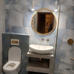 Sur-Bud - Nowoczesna łazienka z marmurowymi płytkami w odcieniach błękitu i szarości, okrągłe lustro w złotej ramie, biała umywalka nablatowa, wisząca toaleta i minimalistyczne oświetlenie.