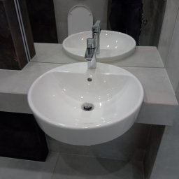 Sur-Bud - Nowoczesna, biała umywalka nablatowa z chromowaną baterią w szarej łazience z widocznym odbiciem osoby robiącej zdjęcie.