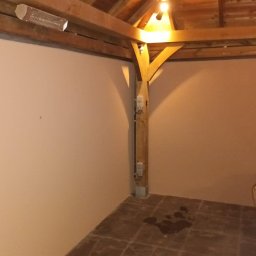 Tomek - Gładkie, pomalowane ściany altany z drewnianą konstrukcją w Lubaczowie. Widoczna lampa grzewcza i plama na podłodze. Praca po szpachlowaniu i malowaniu.