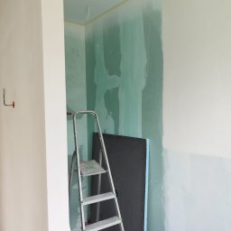 Tomek - Ściana w trakcie szpachlowania z widoczną drabiną i płytą izolacyjną. Fragment instalacji elektrycznej na ścianie. Prace przygotowawcze w pomieszczeniu przed wykończeniem.