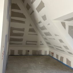 Tomek - Pokój na poddaszu w trakcie prac wykończeniowych: ściany i sufit z fragmentami płyt gipsowo-kartonowych, zabezpieczona podłoga, widoczne puszki elektryczne.