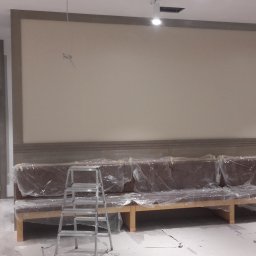 Tomek - Wnętrze w trakcie prac: zabezpieczona folią sofa, drabina, ściana przygotowana do malowania z widocznymi przewodami oświetleniowymi.