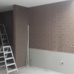 Tomek - Brązowa ściana z płytek w połowie wykończona, widoczna drabina i wystające kable. Przygotowanie do wykończenia wnętrza, remont łazienki lub kuchni.