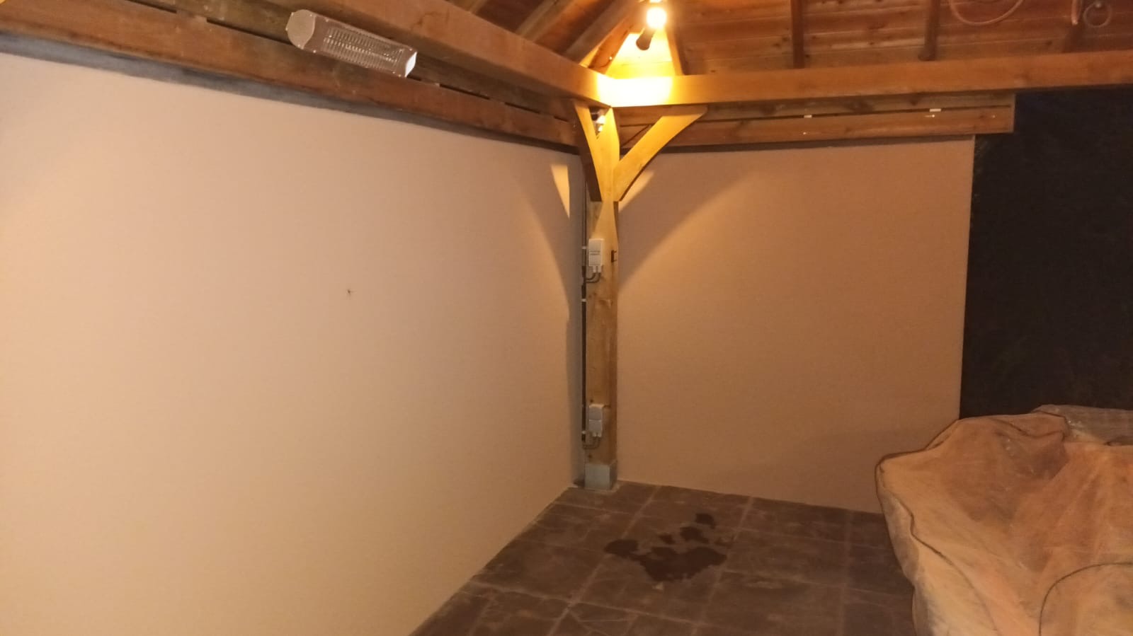 Gładkie, pomalowane ściany altany z drewnianą konstrukcją w Lubaczowie. Widoczna lampa grzewcza i plama na podłodze. Praca po szpachlowaniu i malowaniu.