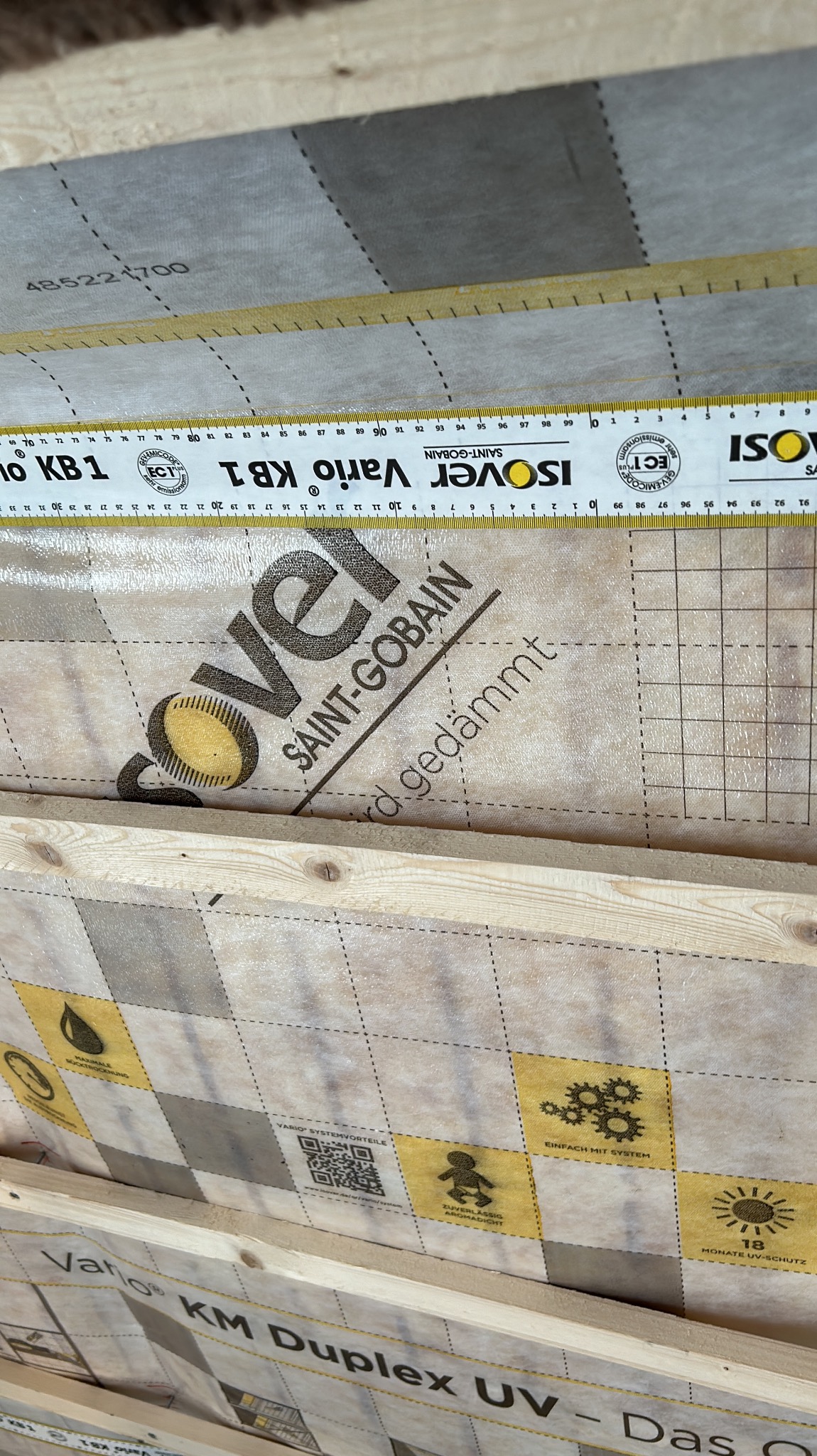 Izolacja poddasza z folią paroizolacyjną Isover Vario KB1, widoczna miarka. Elementy konstrukcji drewnianej. Detal montażu.