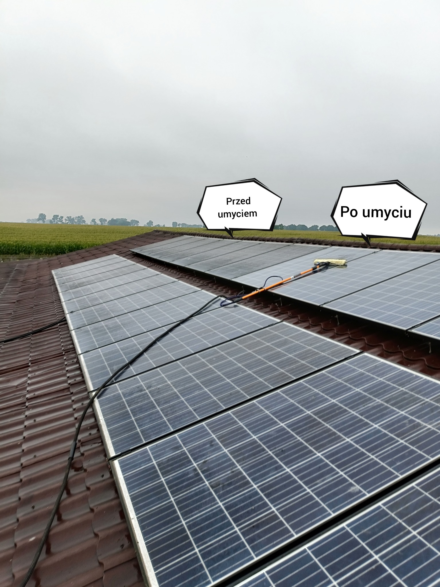 Panele słoneczne na dachu, część umyta, część zabrudzona, z widocznym narzędziem do czyszczenia, w tle pole uprawne.